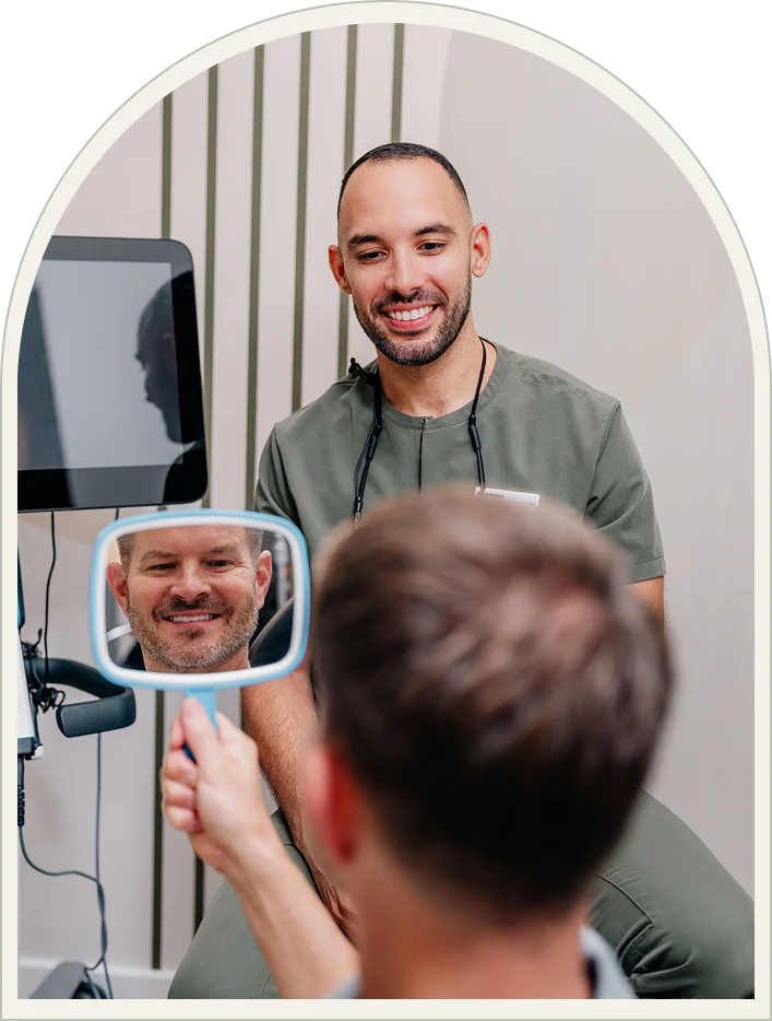 A patient viewing their smile in a hand mirror with the Enamyl Dentistry team